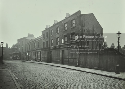St Marychurch Street, Rotherhithe. A row of buildings with boarded-up shop fronts and a wooden fence, c1914.  X.png
