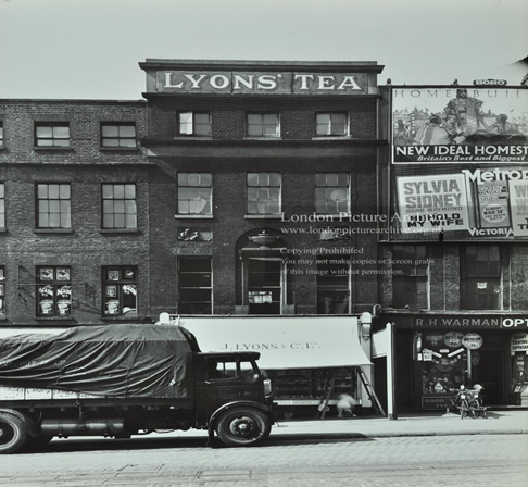Blackfriars Road, c1935. J Lyons Tea House at number 7. At number 6, with a bicycle rack in front, is R.H. Warman opticians. Notice the cobbled road with tram tracks. X..png