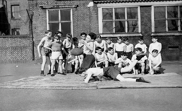 Grange Road. Boys at the Bacon School, Bermondsey, practice rugby tackling in the school yard.  X..png