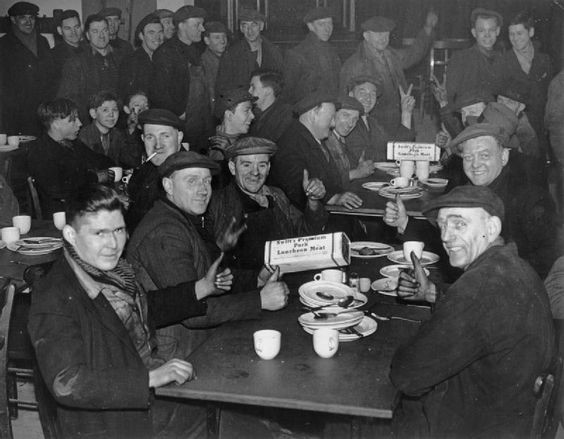Dock workers give the thumbs up and V signs as they lunch on American canned meat at a London Dockworkers Canteen, London, 1941..jpg