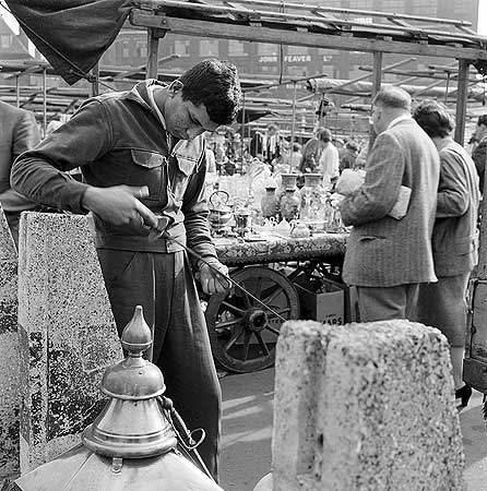 Bermondsey Antiques Market. A young man examining a sword, with the John Feaver factory on Tower Bridge Road visible in the background.  X.png