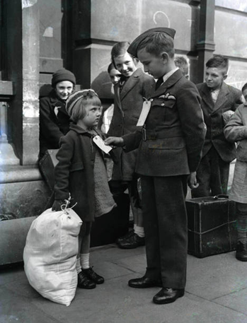 World War Two, 10th, September 1942. Brian Lee wearing his RAF uniform studies the evacuation label on a, model evacuee, Alice King aged 5, from Rotherhithe.  X.png